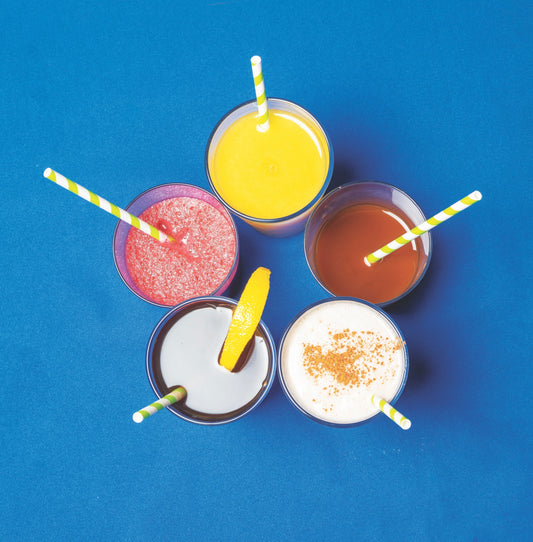An overhead shot of 5 colorful drinks on a blue backdrop