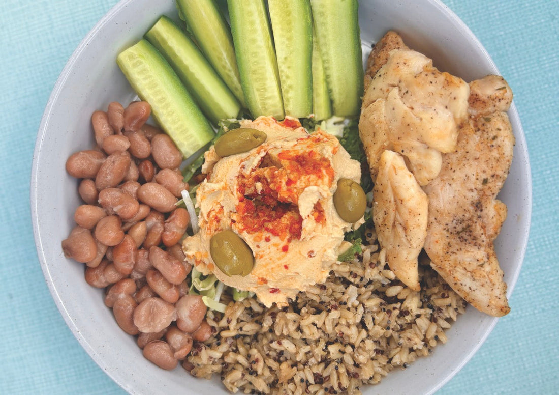 A meal of chicken, beans, rice, cucumber sticks and hummus assembled in a bowl