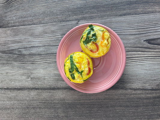 Two egg bites with chopped spinach and sweet peppers resting on a pink plate